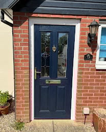 Dark blue front door with glass panels on a brick building, flanked by windows and potted plants
