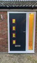 Modern dark gray front door with yellow panels on a red brick house with white frame