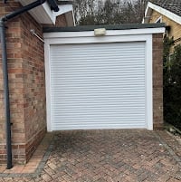 White roller garage door with metal frame attached to brick wall, viewed from driveway