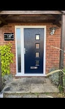 Dark blue front door with two small windows on a red brick house exterior, with green ivy and potted plant visible