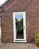 White framed door on a red brick wall with green foliage visible through the window pane