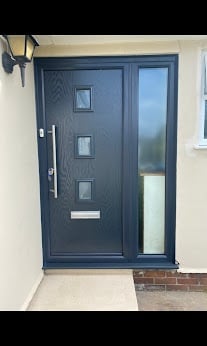 Modern dark blue front door with three square windows and a glass panel sidelight on a white wall