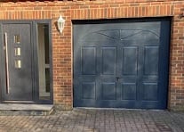 Dark blue garage door and black front door on a red brick house with herringbone patterned driveway