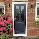 Black front door with white trim on red brick house, flanked by pink flowering shrub