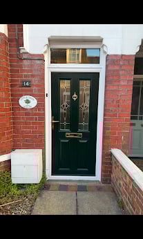 Dark green front door with gold accents on a brick house entrance with fanlight window above