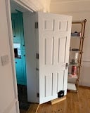 White six-panel interior door standing against hallway wall with turquoise-tinted room visible through doorway