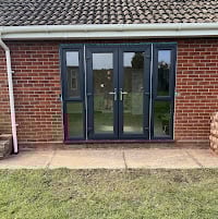 Modern black framed glass bi-fold doors installed in a brick home exterior with green lawn