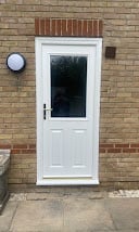 White front door with black window panel on brick building facade with round wall clock above