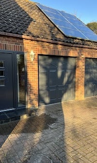Modern brick garage with solar panels installed on the peaked roof and dark garage doors facing a paved driveway