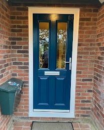 Blue front door with glass panels on a red brick house exterior, with green bin visible