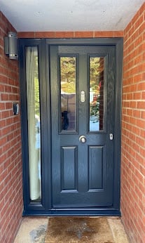 Navy blue front door with glass panels flanked by brick walls and sidelights