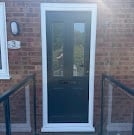 Front entrance with dark green double glass doors, metal railings, and brick exterior wall