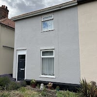 Small white single-story residential house with a dark front door and two windows on the front facade