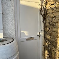 White utility door with metal handle in a concrete basement or service area with exposed pipes and ivy on the wall