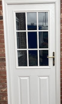 White painted composite door with nine-pane window and brass handle mounted on red brick wall