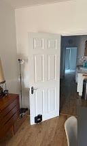 White six-panel interior door in hallway with wooden flooring and furniture visible
