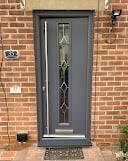 Gray front door with decorative glass panel set into a red brick building exterior