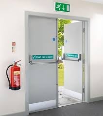 Emergency exit door with green exit sign above, fire extinguisher on left wall, and outdoor view visible through glass