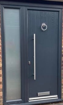 Modern black front door with frosted glass sidelight panel and metal handle on brick wall