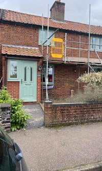 Brick residential building with light blue painted door, yellow window frame, and gravel driveway entrance